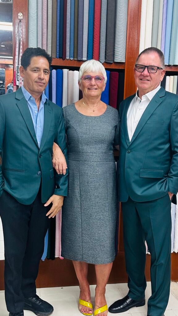 Two happy clients pose with their master tailor, proudly wearing their new bespoke clothing. The men look sharp in perfectly fitted, matching green suits, showcasing the high-quality craftsmanship that distinguishes one of the best tailors in Phuket for custom menswear and womenswear.